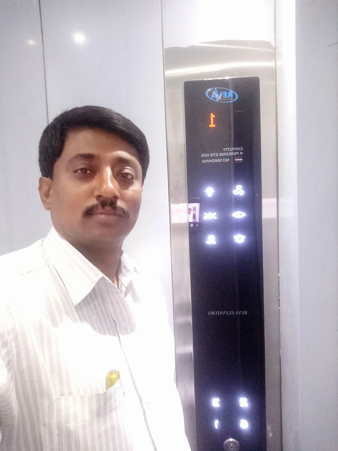 Mr Rudrappa inside an elevator beside a Reva Elevators control panel